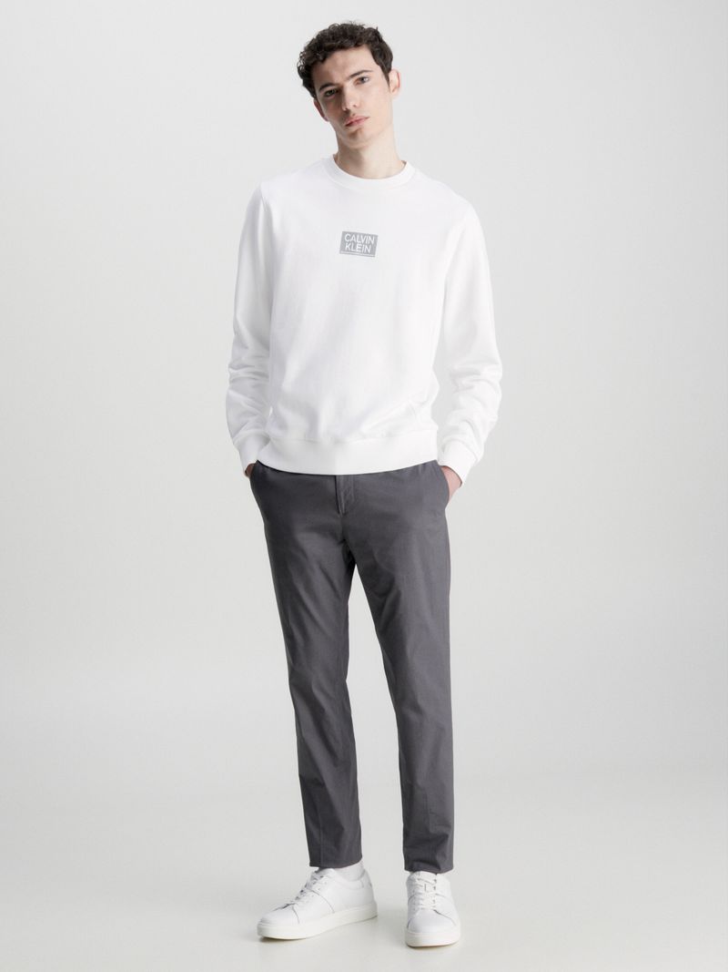 Hombre-con-poleron-blanco-Calvin-Klein-de-manga-larga-cuello-redondo-y-logo-en-el-pecho-combinado-con-pantalon-oscuro.