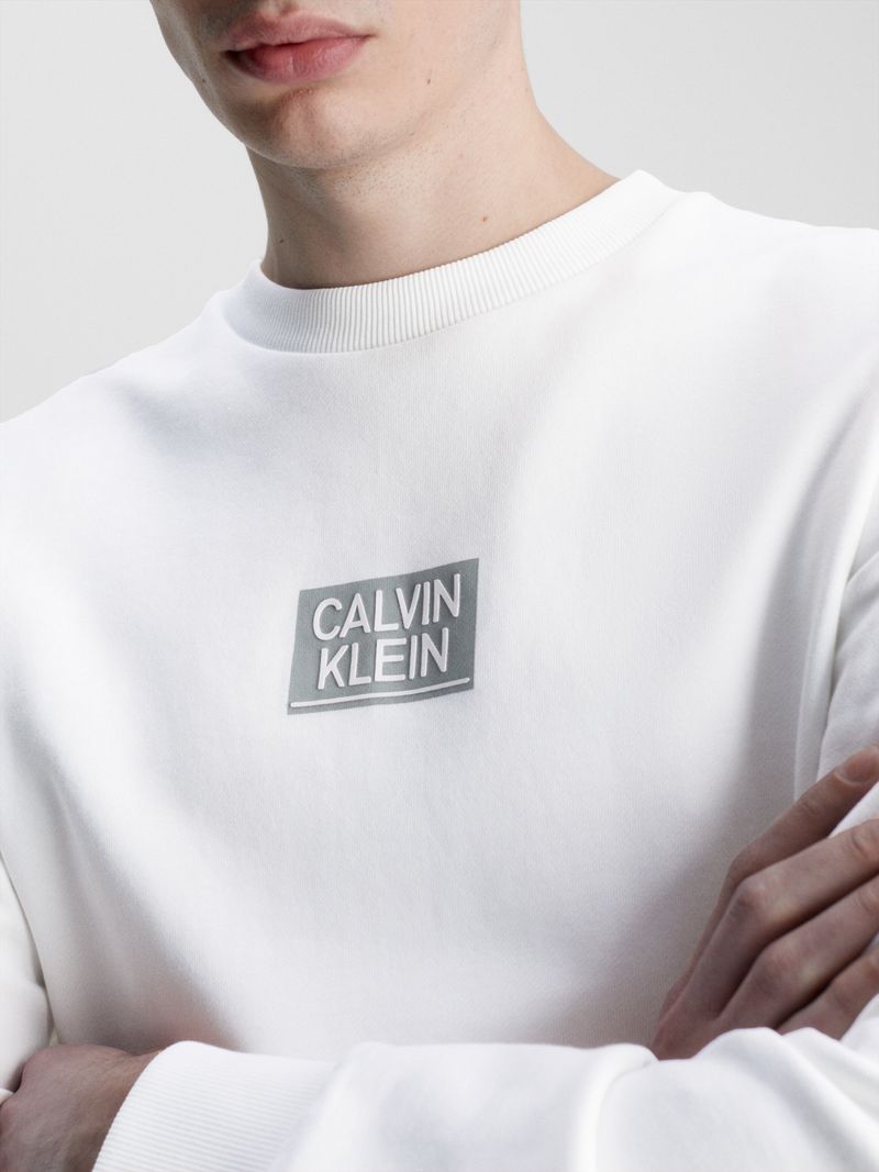 Hombre-con-poleron-blanco-Calvin-Klein-de-manga-larga-cuello-redondo-y-logo-en-el-pecho-combinado-con-pantalon-oscuro.