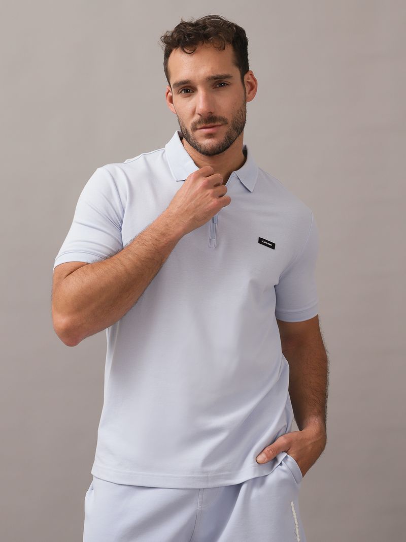 Hombre-con-polo-celeste-y-short-a-juego-de-Calvin-Klein-posa-con-una-mano-en-el-bolsillo-y-otra-en-el-cuello