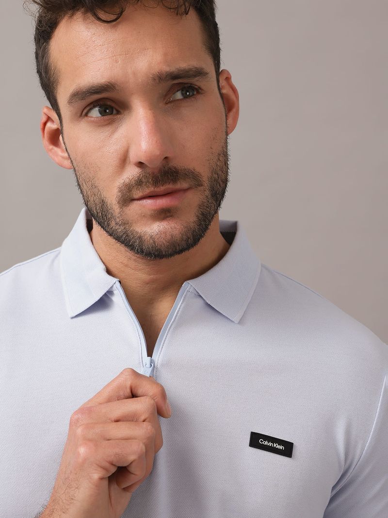 Hombre-con-polo-celeste-y-short-a-juego-de-Calvin-Klein-posa-con-una-mano-en-el-bolsillo-y-otra-en-el-cuello
