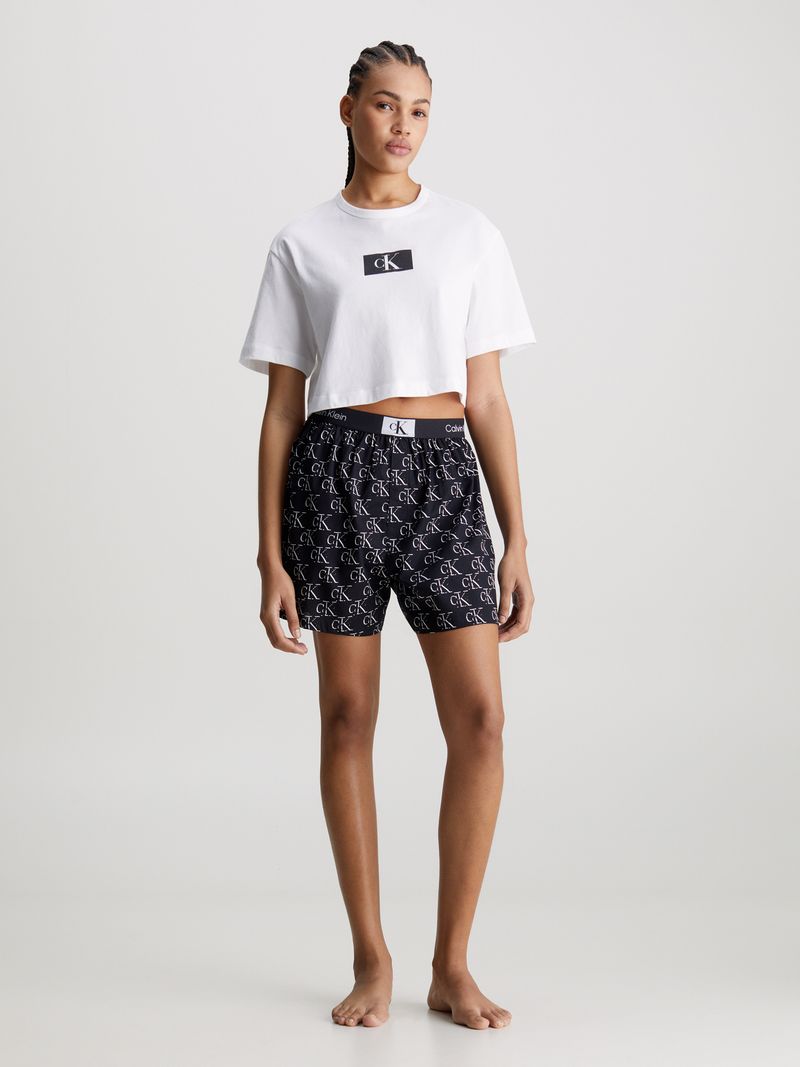 Modelo-luciendo-polera-crop-blanca-Calvin-Klein-combinada-con-shorts-negros-con-logo-CK.