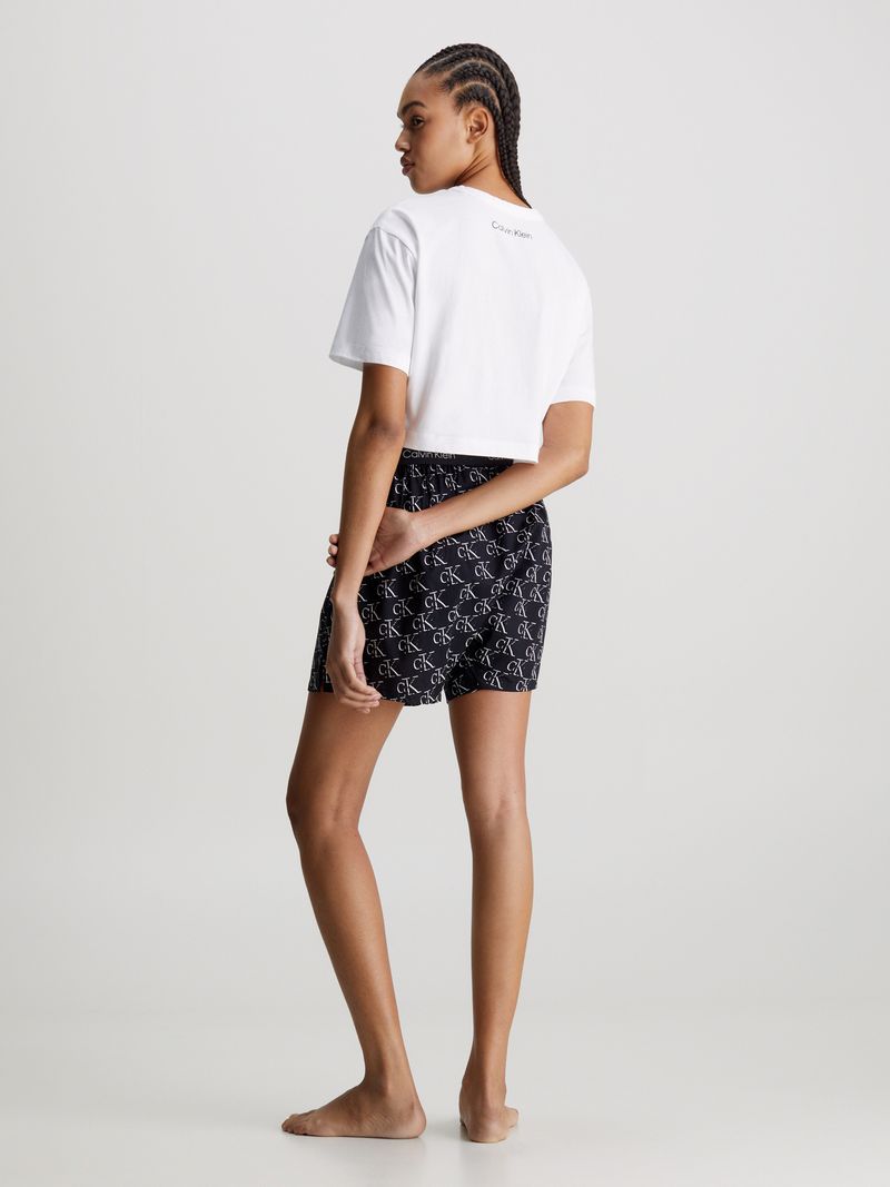 Modelo-luciendo-polera-crop-blanca-Calvin-Klein-combinada-con-shorts-negros-con-logo-CK.
