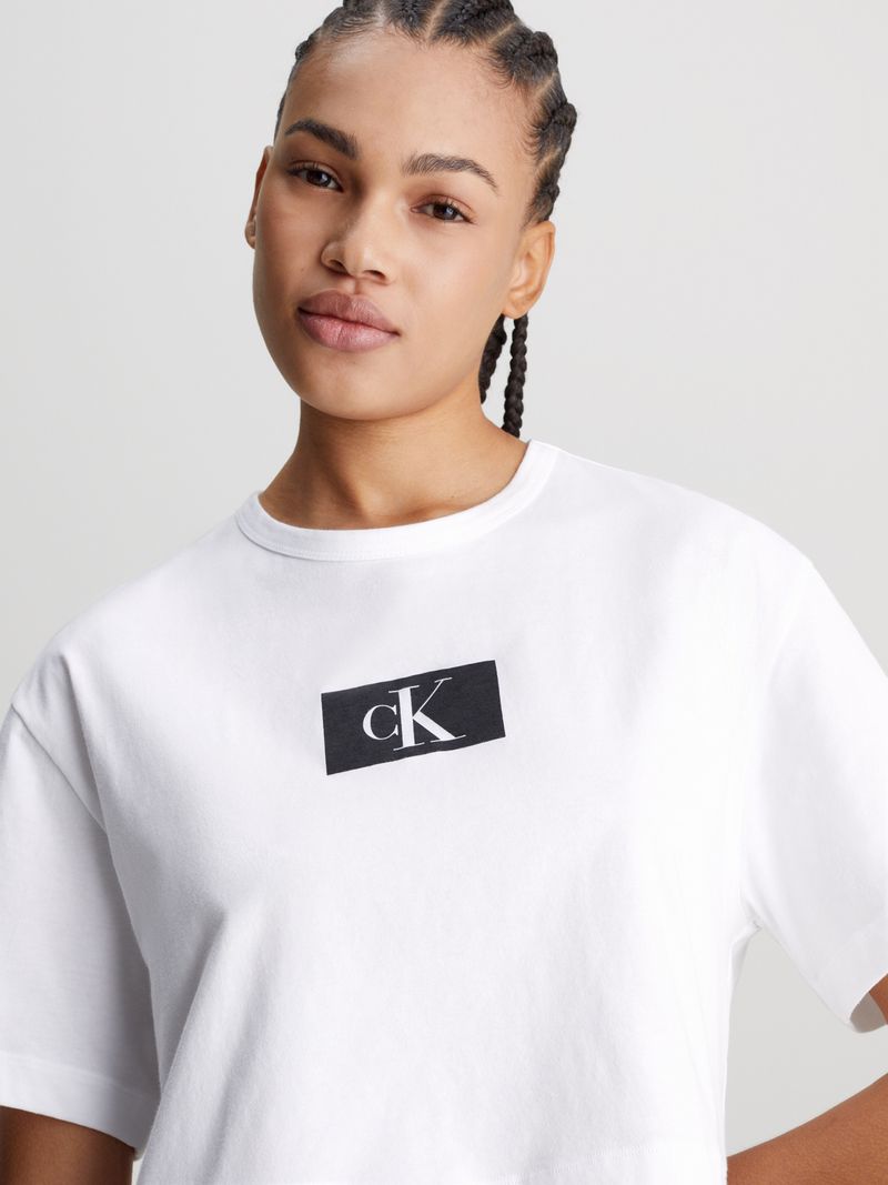 Modelo-luciendo-polera-crop-blanca-Calvin-Klein-combinada-con-shorts-negros-con-logo-CK.