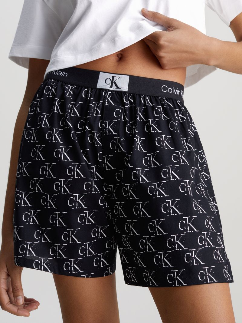 Modelo-luciendo-polera-crop-blanca-Calvin-Klein-combinada-con-shorts-negros-con-logo-CK.