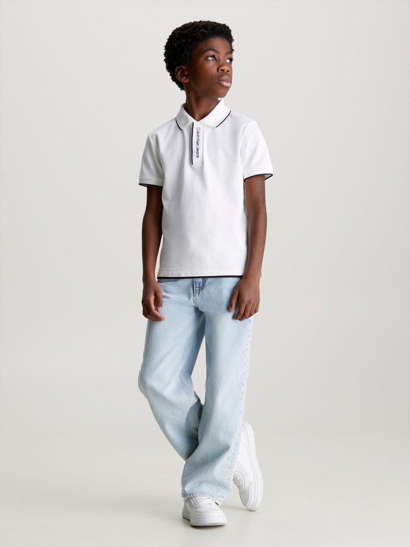 Niño-con-polera-polo-blanca-y-jeans-celestes-de-Calvin-Klein-posa-con-una-expresion-pensativa