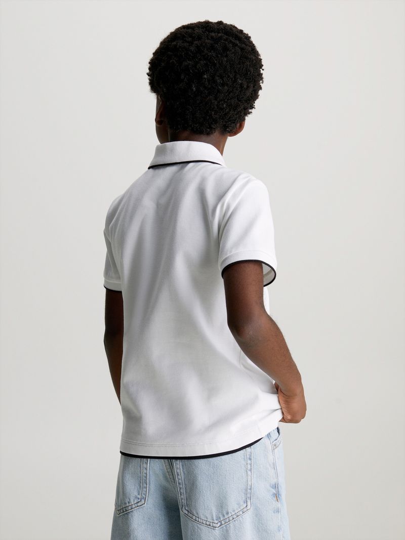 Niño-con-polera-polo-blanca-y-jeans-celestes-de-Calvin-Klein-posa-con-una-expresion-pensativa