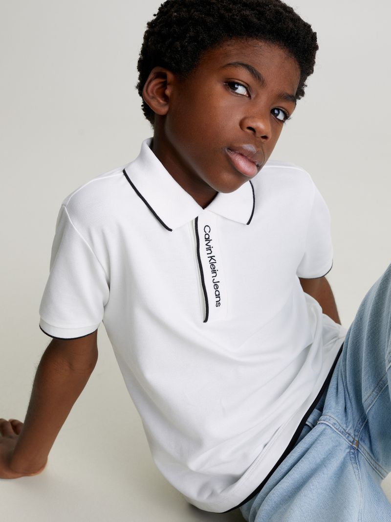 Niño-con-polera-polo-blanca-y-jeans-celestes-de-Calvin-Klein-posa-con-una-expresion-pensativa